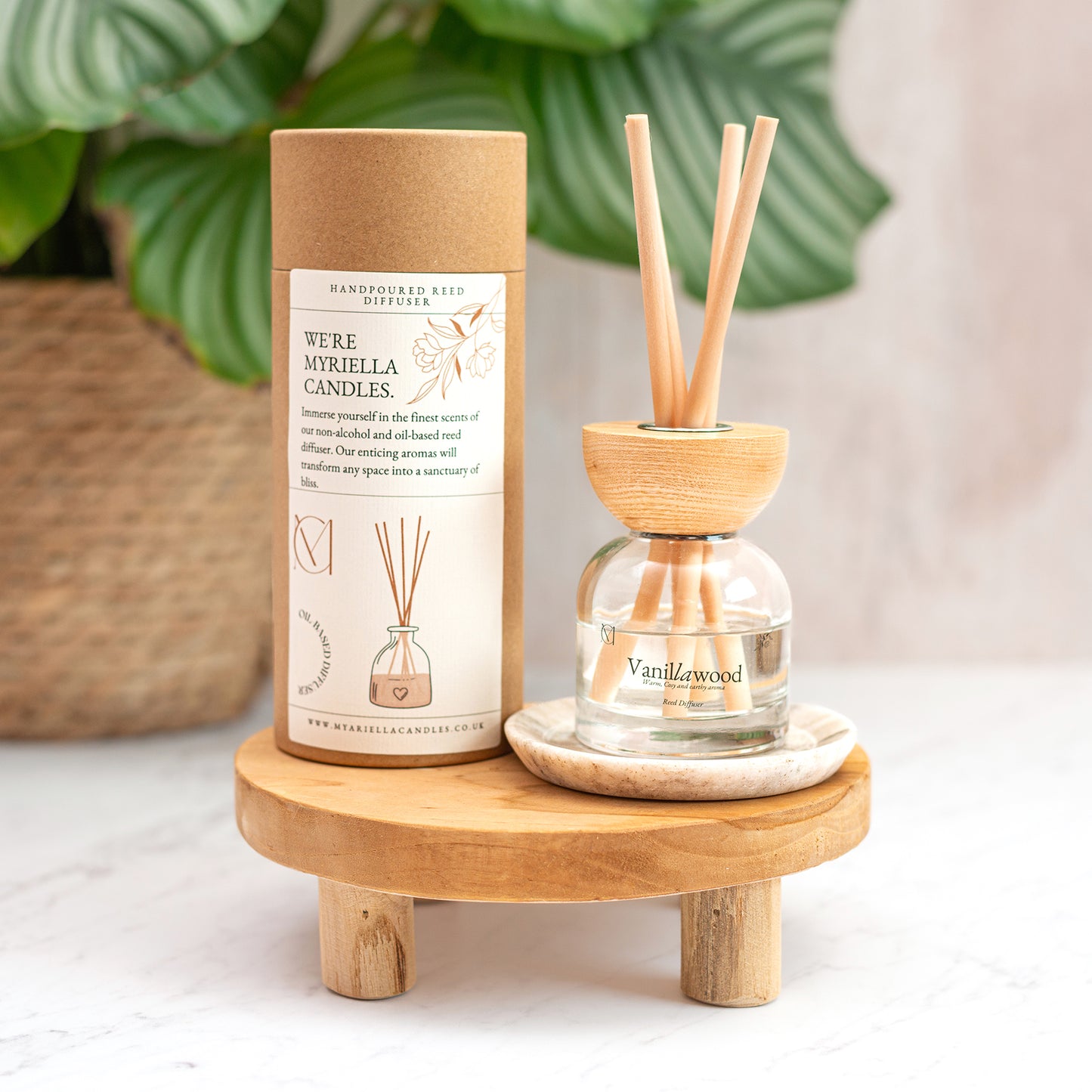 Vanilla sandalwood diffuser with packaging on a wooden stand with a plant in the background. Vanilla Sandalwood Reed Diffuser 100ml by Myariella Candles, luxury handmade home fragrance in Dundee UK
