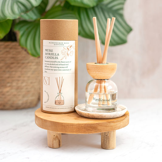 Vanilla sandalwood diffuser with packaging on a wooden stand with a plant in the background. Vanilla Sandalwood Reed Diffuser 100ml by Myariella Candles, luxury handmade home fragrance in Dundee UK