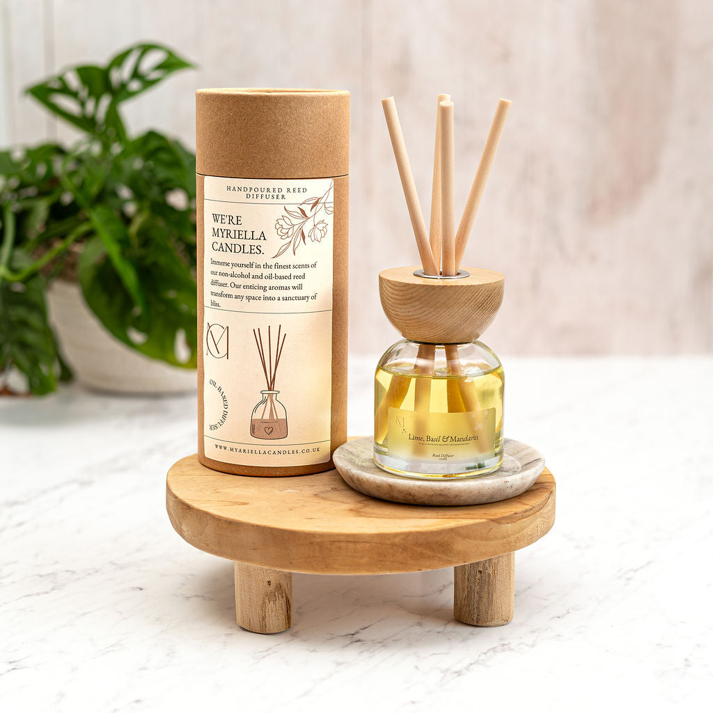 A luxury glass reed diffuser bottle with Lime Basil and Mandarin fragrance oil and natural rattan reeds, set against a modern home interior background.
